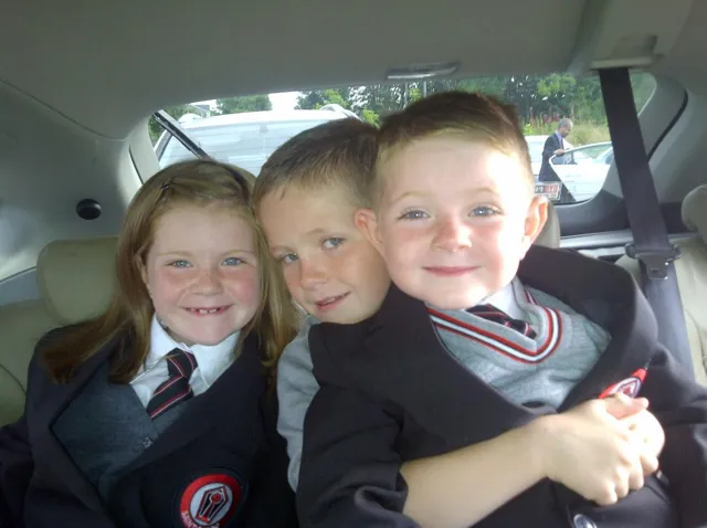 Joshua Adams as a young pupil in his school uniform, sitting in the back of a car with two other children